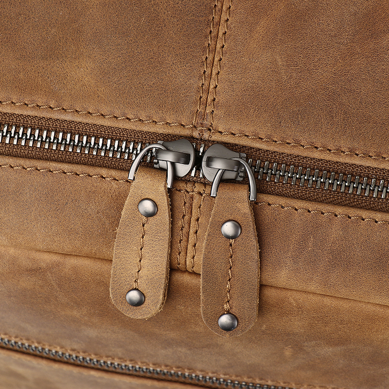 This close-up captures the double-zip detail of a brown crazy horse leather bag, highlighting metal zipper teeth, leather pull tabs reinforced with metal rivets, and neat stitching that fuses exquisite craftsmanship with vintage ruggedness.